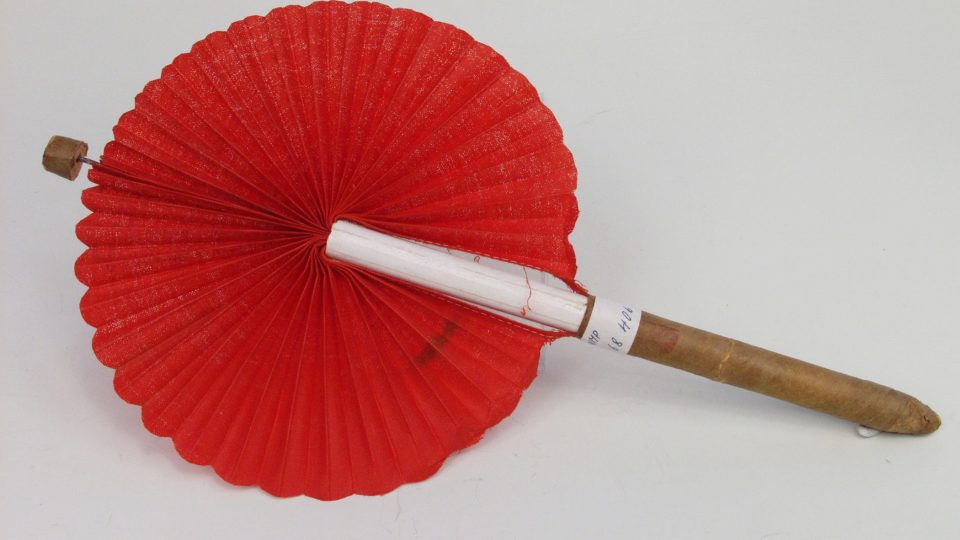 Vějíř tubový skládací kokardový s textilním listem. List tvoří impregnované plisované plátno červené barvy