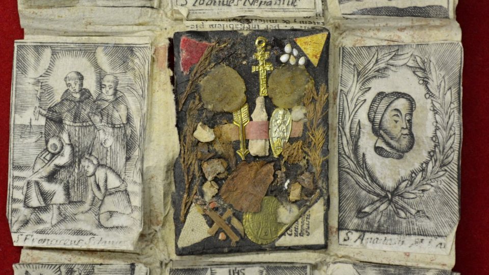 Vnější škapulířové pouzdro, zdrobené dracounovým monogramem „IHS“ spolu s vnitřním papírovým balíčkem s milostným obrazem Panny Marie z farního kostela Jana Křtitele v bavorském Wessobrunu a vyobrazením sv. Antonína Paduánského