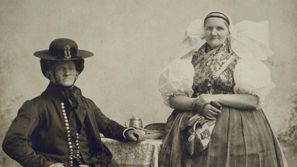 Historická fotografie páru v plzeňském kroji – vdaná žena s manželem (holubice se „zalomenými“ křídly pro vdanou ženu)