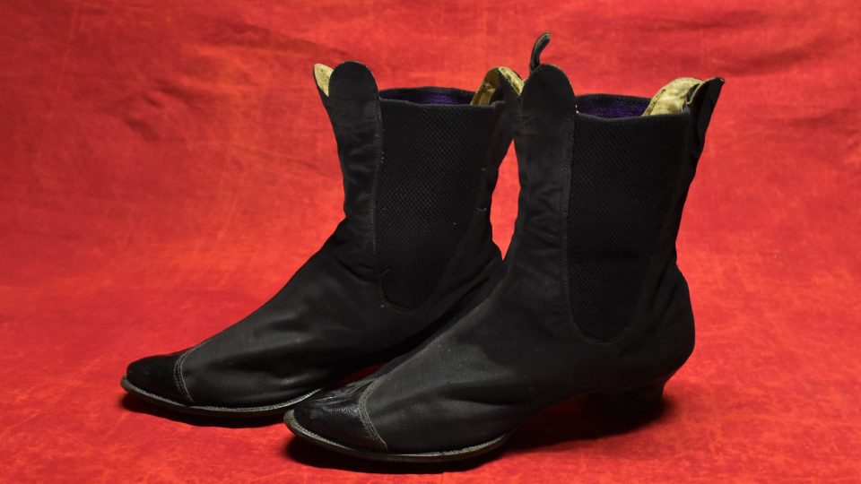 Dámské černé boty – perka s lakovou špičkou na polovysokém podpatku, s koženou podrážkou. Na kotnících klínky z gumy. Kolem roku 1890