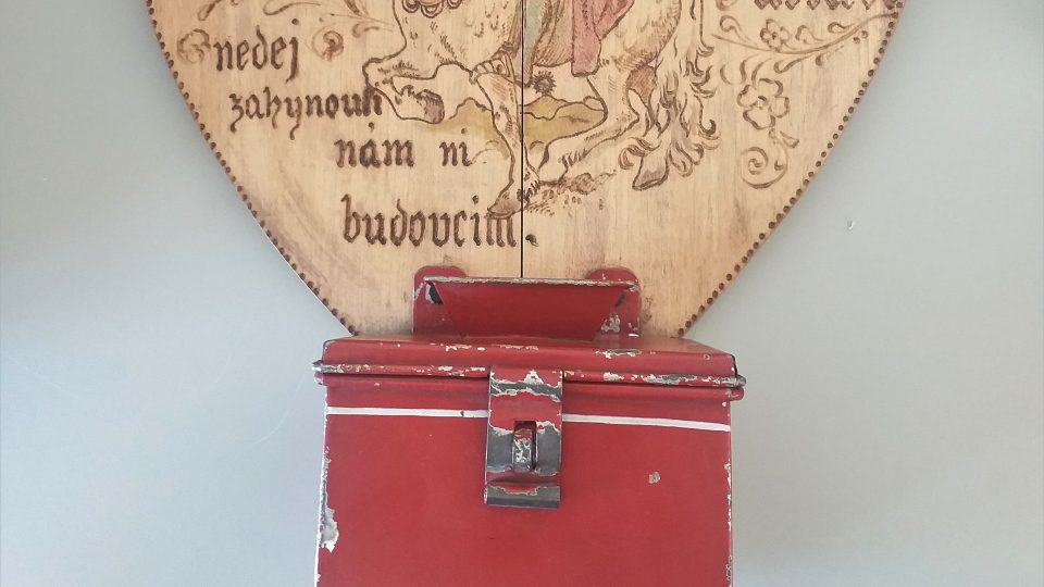 Plechová pokladnička s dřevěnou deskou, na které je vypálený reliéf svatého Václava. Vytvořili žáci školy pro mrzáčky v Plzni roku 1914
